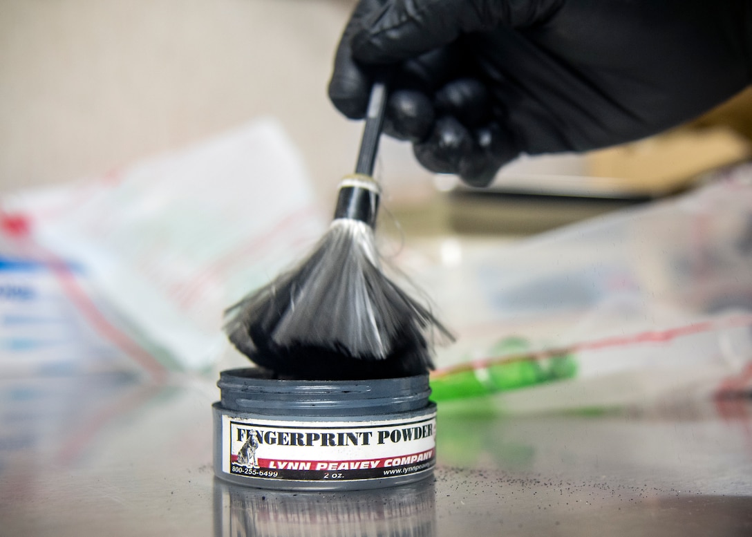 An investigator from the 23d Security Forces Squadron dabs a brush in fingerprint powder during crime scene investigation, June 26, 2019, at Moody Air Force Base, Ga. After arriving at a crime scene, investigators are responsible for the examination, collection and transportation of evidence for further inspection. Once evidence is thoroughly inspected it will be cross-referenced with the suspects DNA along with the victim’s statements to help determine if they committed a crime. (U.S. Air Force photo by Airman 1st Class Eugene Oliver)