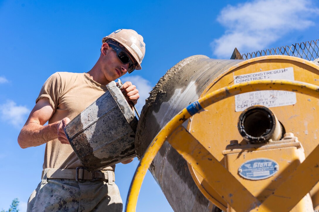 A sailor is seen from a low angle pouring material into a construction machine.