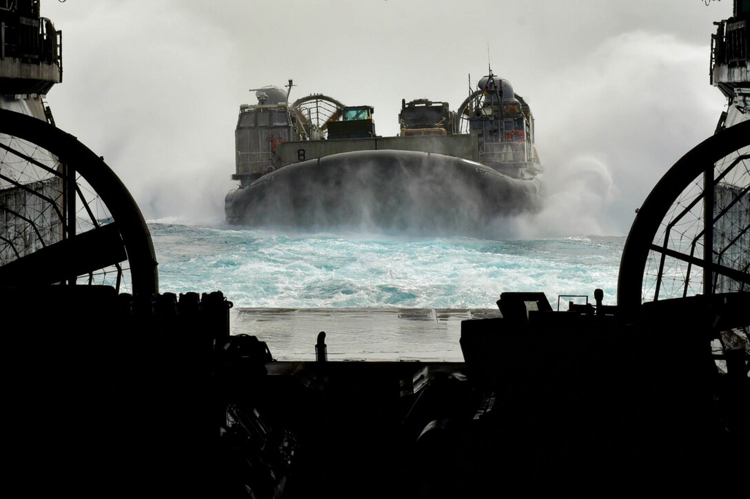 An air-cushioned landing craft in the water about to enter the well deck of a ship.