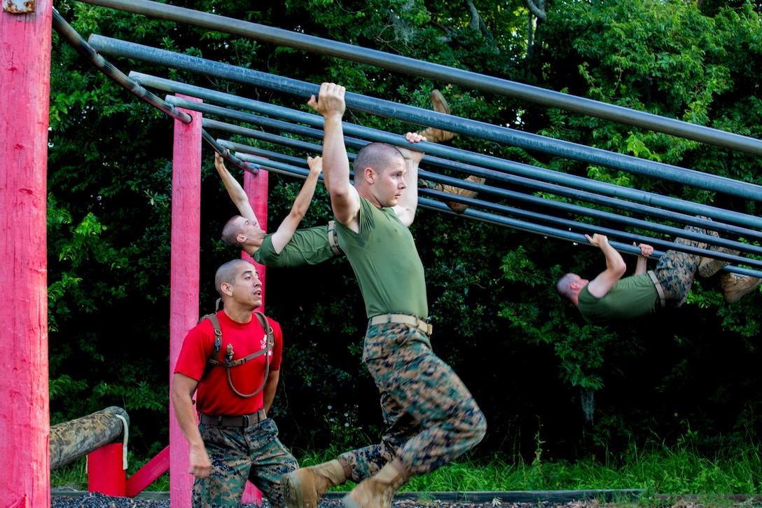 Marines slide down angled poles during an obstacle course.