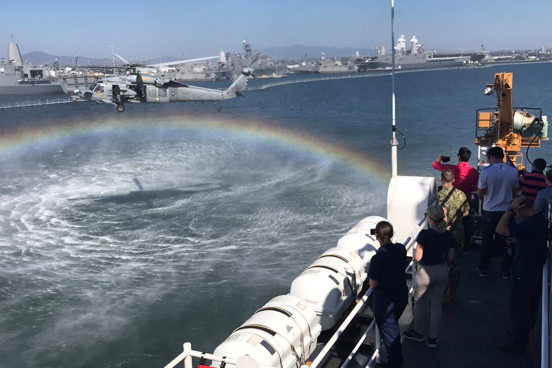 People on deck of cutter watch helicopter.