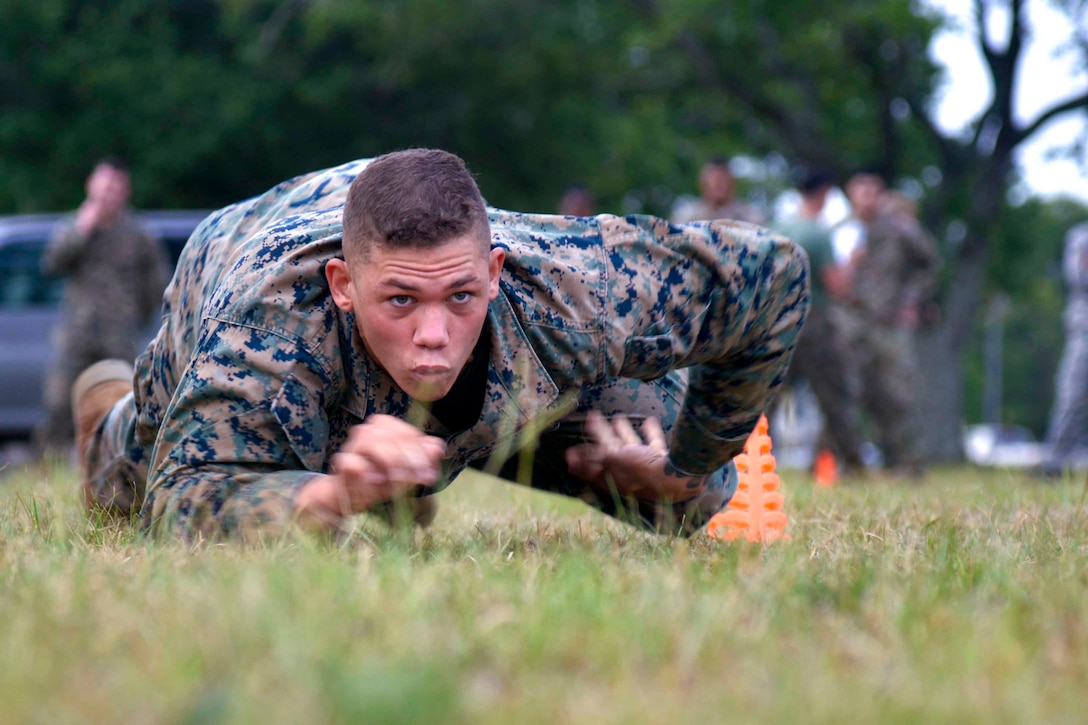 A Marine crawls along grass.