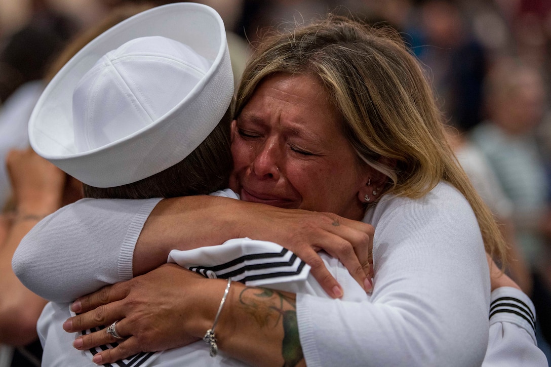 A loved one cries while hugging a sailor in dress whites.