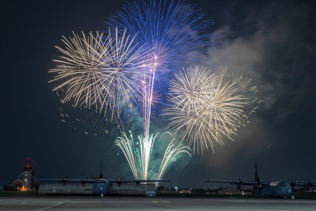 Fireworks explode above two military aircraft at night.