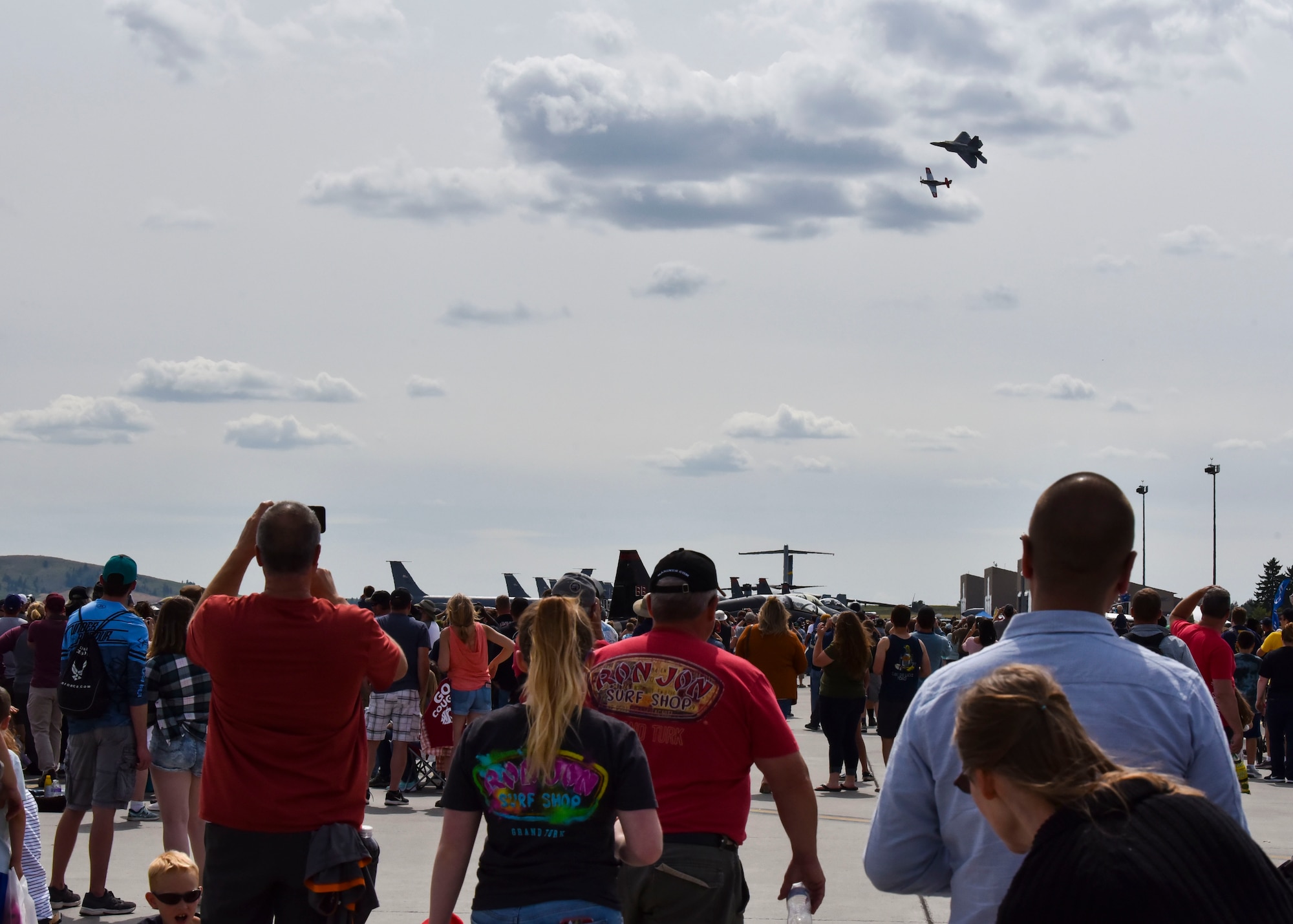 People at the 2019 Skyfest Open House and Airshow  watch a F-22 Raptor and a P-51 Mustang, on the flight line of Fairchild Air Force Base, Washington, June 22, 2019. Fairchild opened its gates to the public for a free one-day event to showcase Pacific Northwest airpower and U.S. Air Force capabilities. The airshow included the F-22 Demonstration Team, U.S. Army Golden Knights and 11 other aerial acts. (U.S. Air Force photo by Airman Kiaundra Miller)