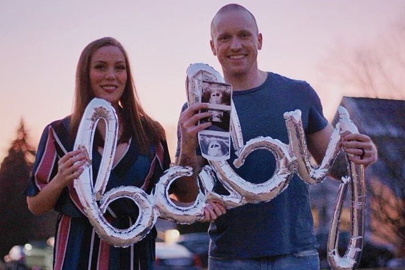 Man and pregnant woman stand while holding a baby balloon.