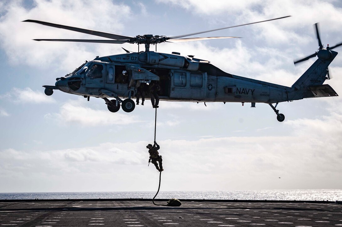 A Marine slides down a rope out of a helicopter.