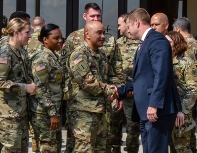 US Army soldiers shake hands with a man in a suit.
