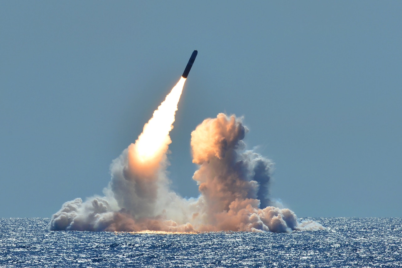 A missile launches from the ocean amid clouds of smoke.