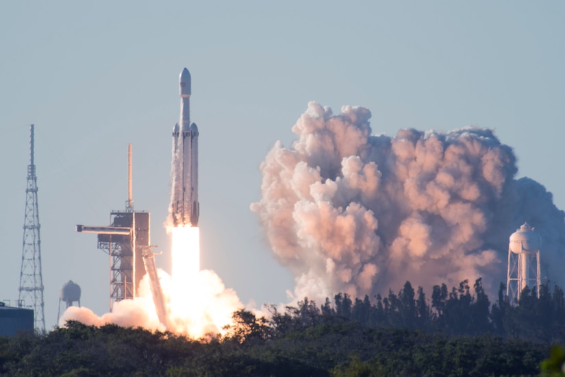 A rocket launches from the ground. A large billow of smoke billows out from the bottom of the rocket.