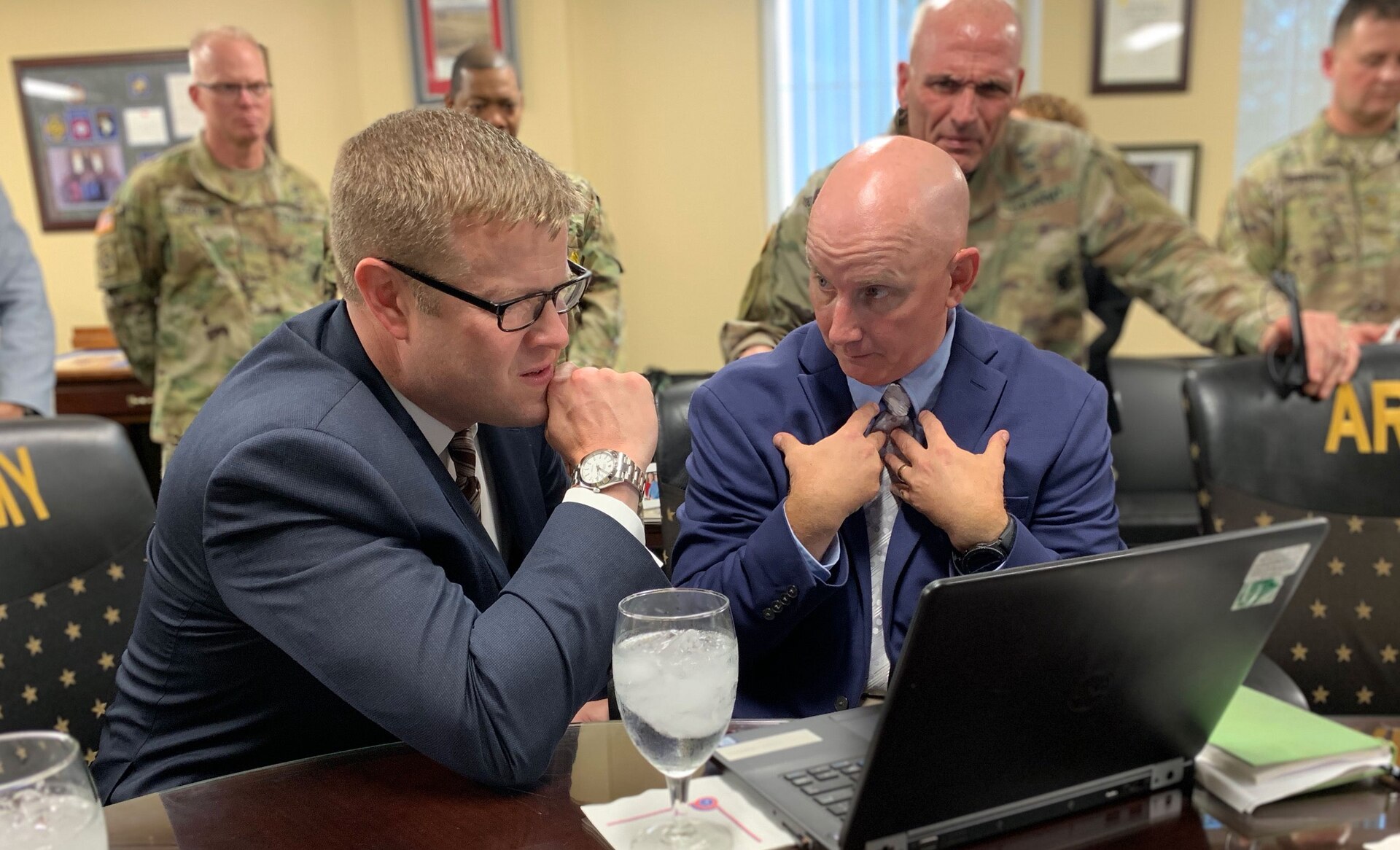 man in a suit looks at a laptop with another man in a suit.