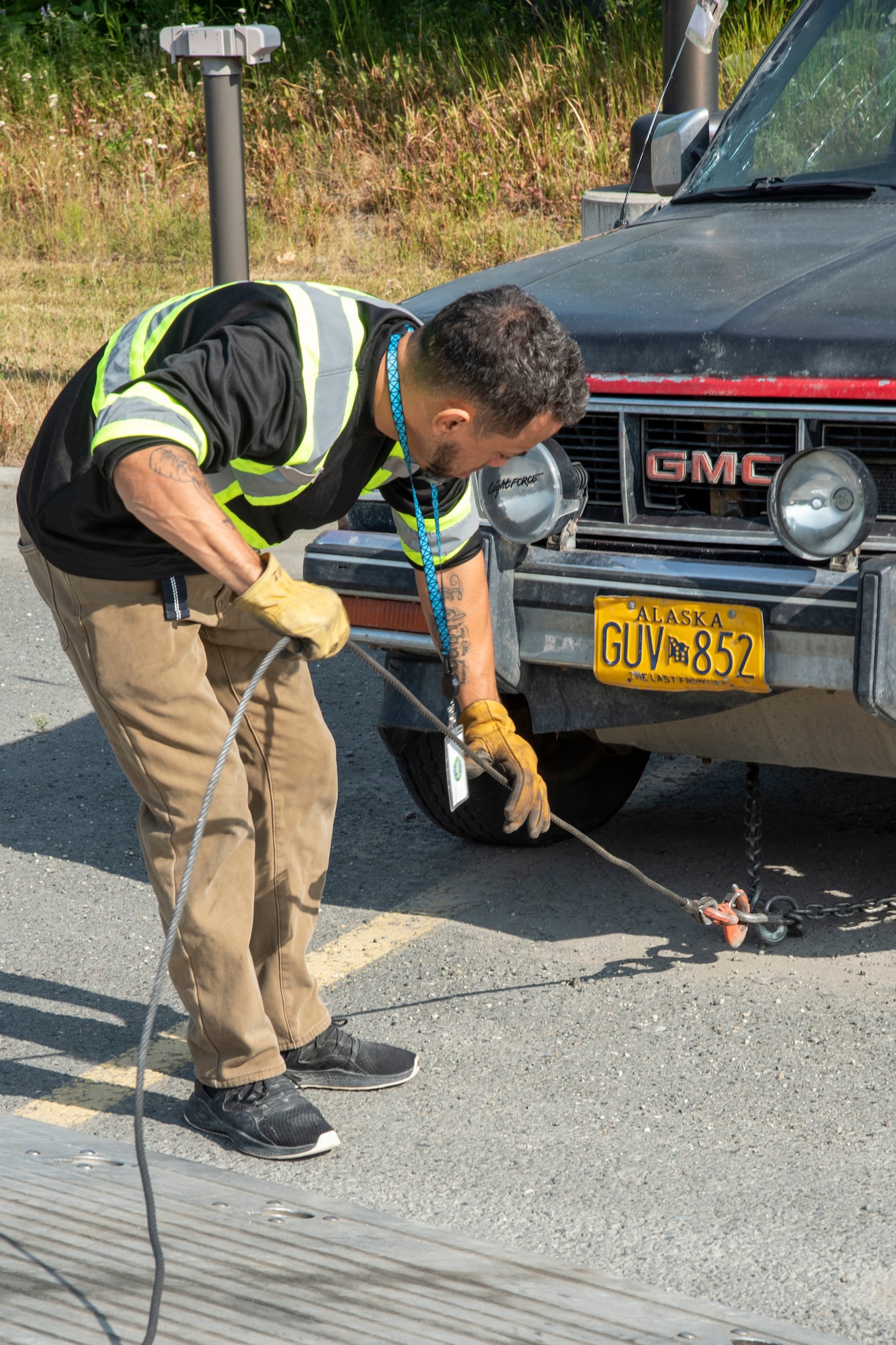 Edison Minyatty, an assistant tow truck operator with JT Towing LLC, adjusts chains attached to a vehicle July 1, 2019, on Joint Base Elmendorf-Richardson, Alaska. Abandoned and illegally parked vehicles on Joint Base Elmendorf-Richardson, Alaska, are towed because they present safety hazards.