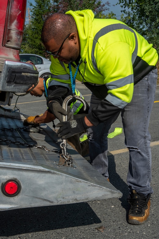 Edison Minyatty, an assistant tow truck operator with JT Towing LLC, and Jonathan Mejia, owner of JT Towing, secure a vehicle to a tow truck with chains July 1, 2019, on Joint Base Elmendorf-Richardson, Alaska. Abandoned and illegally parked vehicles on Joint Base Elmendorf-Richardson, Alaska, are towed because they present safety hazards.