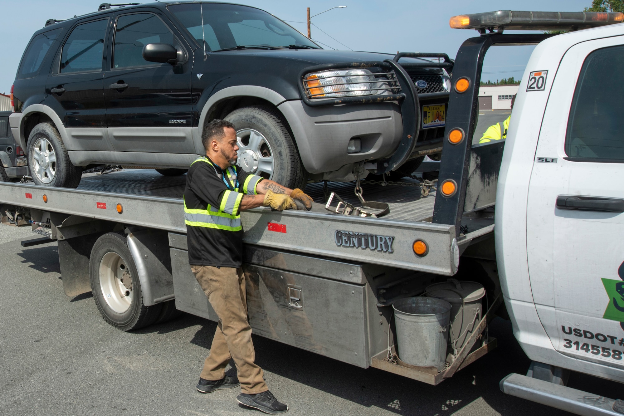 Edison Minyatty, an assistant tow truck operator with JT Towing LLC, tightens a strap to secure a vehicle to a tow truck July 1, 2019, on Joint Base Elmendorf-Richardson, Alaska. Abandoned and illegally parked vehicles on Joint Base Elmendorf-Richardson, Alaska, are towed because they present safety hazards.