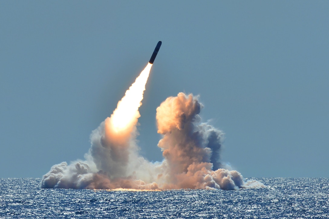 A missile launches from the ocean amid clouds of smoke.