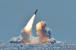 A missile launches from the ocean amid clouds of smoke.