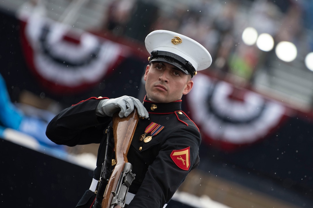 A marine in uniform holds a gun during a ceremony.