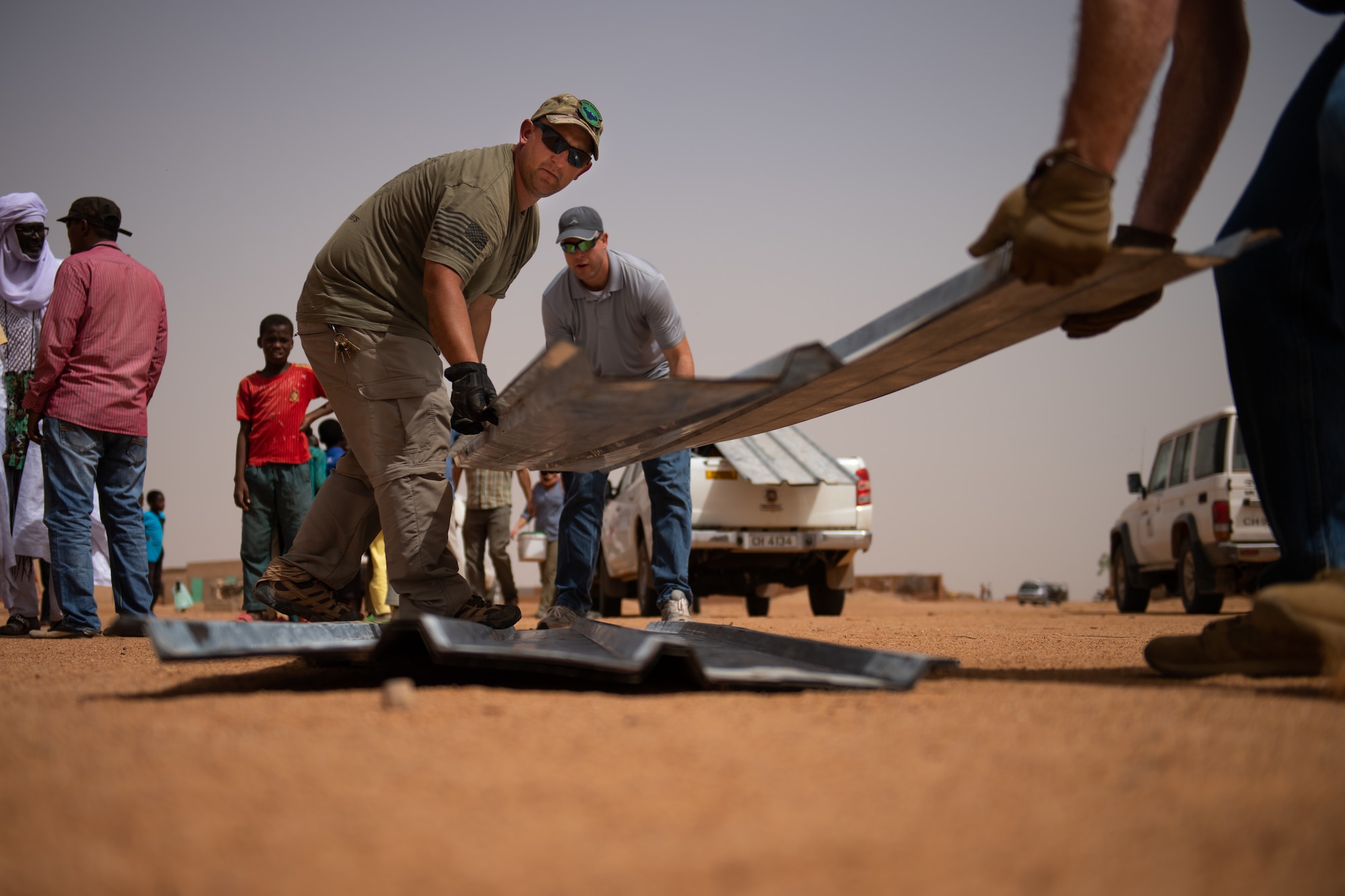 U.S. Air Force Tech. Sgt. Kelly Warren, 724th Expeditionary Air Base Squadron civil engineer flight structural craftsman; Staff Sgt. Jacob Johnson, 435th Air Expeditionary Wing chaplain assistant; and Senior Master Sgt. Adam Liby, 724th EABS CEF superintendent, place a sheet of tin roofing on the ground at a village in Agadez, Niger, June 27, 2019. The civil engineer Airmen installed the roofing on a classroom they built for the village. (U.S. Air Force photo by Staff Sgt. Devin Boyer)