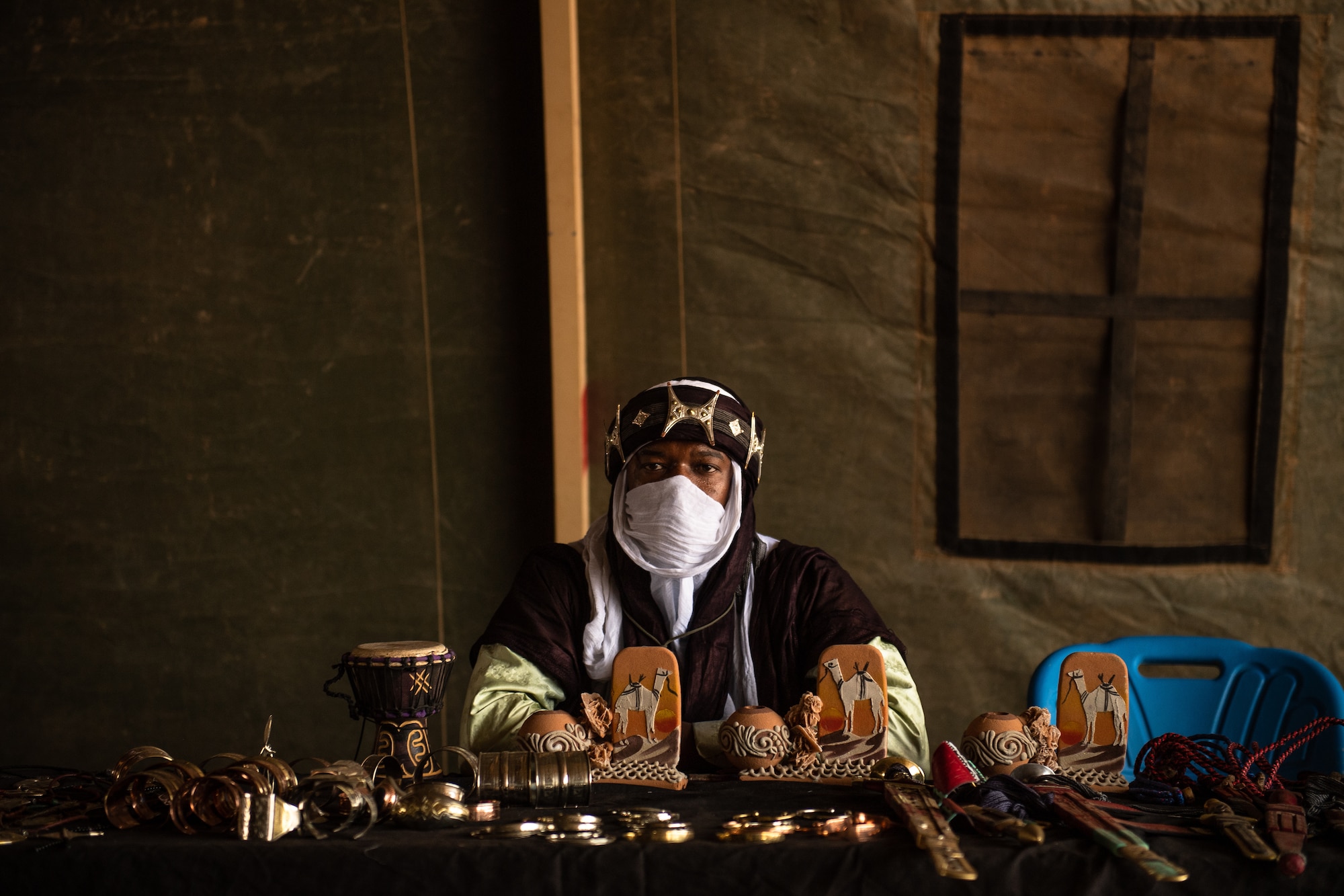 A vendor sits behind a table of hand-made souvenirs during a bazaar at Nigerien Air Base 201 in Agadez, Niger, June 30, 2019. The bazaar hosted 43 vendors selling bracelets, masks, blankets, bags, and various other souvenirs. (U.S. Air Force photo by Staff Sgt. Devin Boyer)