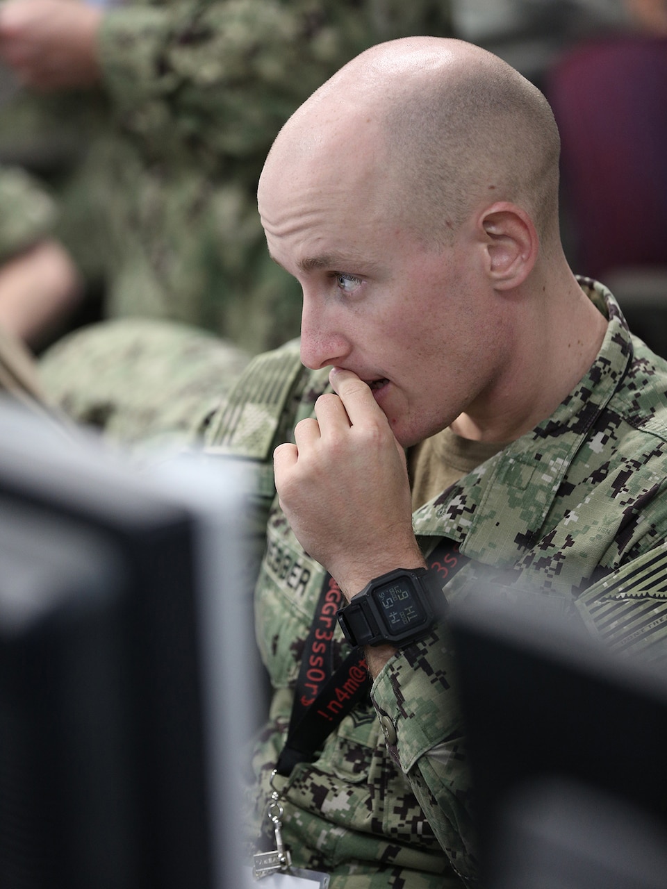 A lone uniformed service member reads a computer screen.  His fingers are pressed to his lips, and he appears concerned.