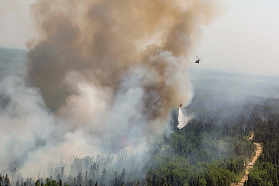 A helicopter flies over smokey wildfire.