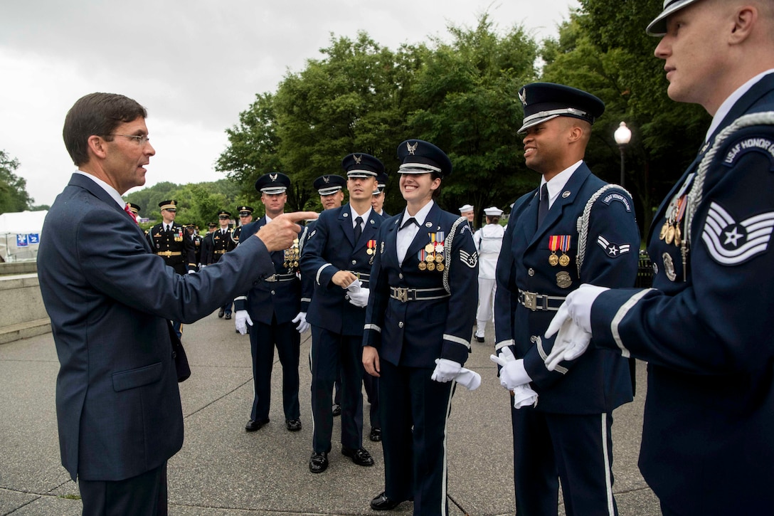 Acting Defense Secretary Dr. Mark T. Esper talks with a group of smiling airmen outside.