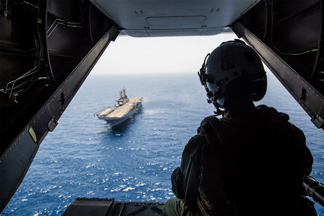 A Marine looks out at the ocean from the back of an aircraft.