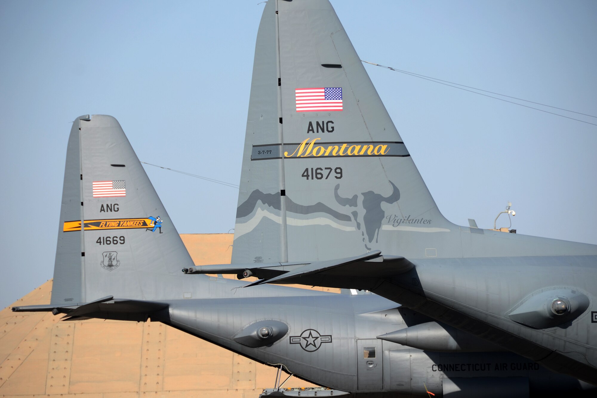 U.S. Air Force C-130s from the Montana and Connecticut Air National Guard currently assigned to the 386th Air Expeditionary Wing sit side by side on the tarmac at Ali Al Salem Air Base, Kuwait, July 3, 2019. The units are currently deployed here providing tactical airlift to the Central Command Area of Responsibility. (U.S. Air National Guard photo by Capt. Stephen Hudson/Released)