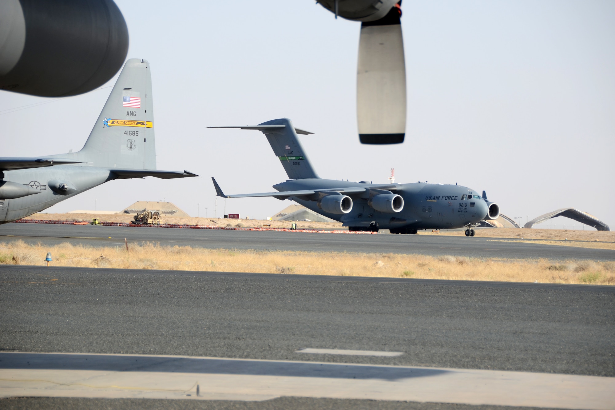 A C-17 Globe Master III taxis past a C-130 Hercules at Ali Al Salem Air Base, Kuwait, July 3, 2019. The units are currently deployed here providing tactical airlift to the Central Command Area of Responsibility. (U.S. Air National Guard photo by Capt. Stephen Hudson/Released)