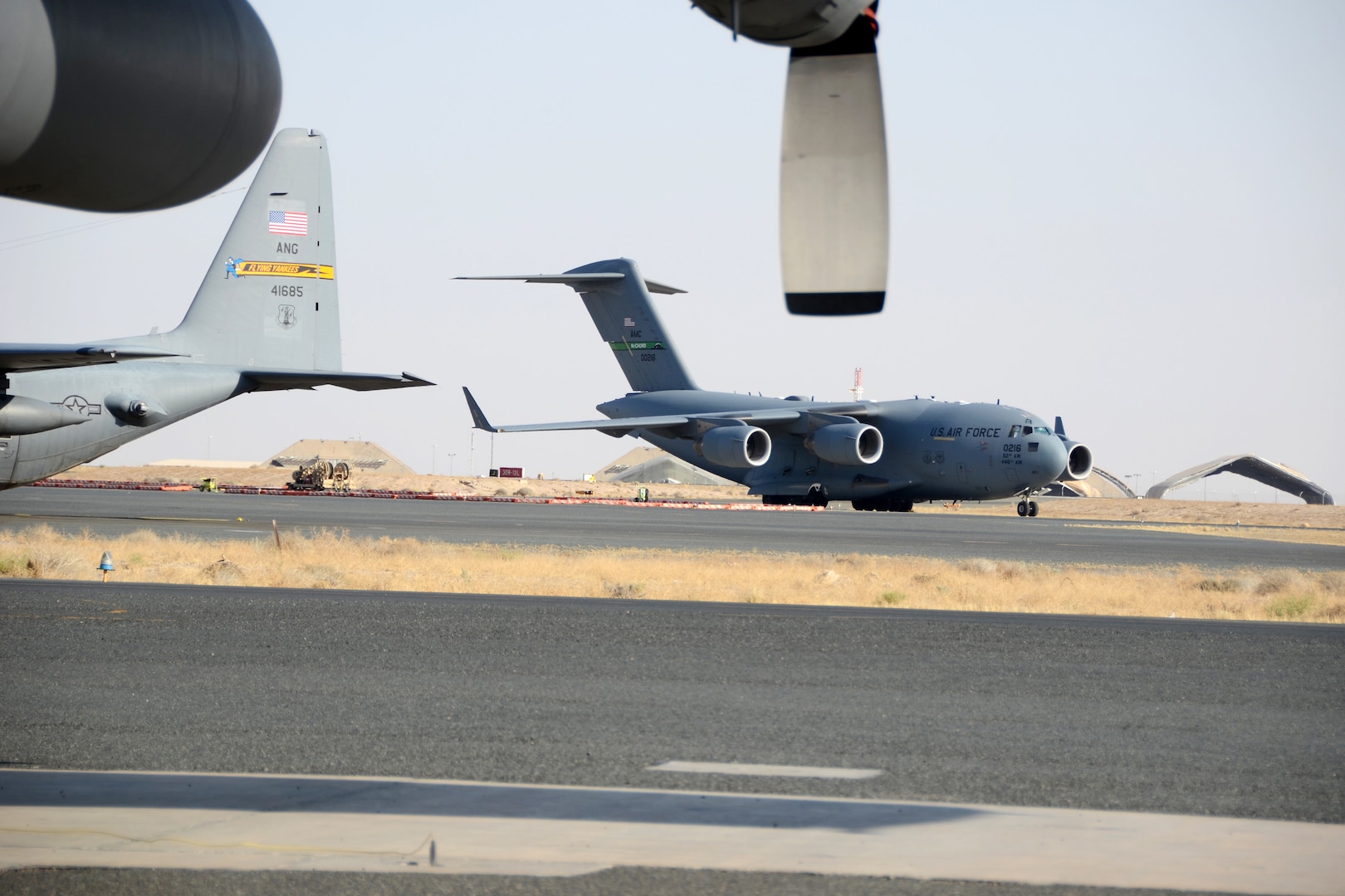 A C-17 Globe Master III taxis past a C-130 Hercules at Ali Al Salem Air Base, Kuwait, July 3, 2019. The units are currently deployed here providing tactical airlift to the Central Command Area of Responsibility.