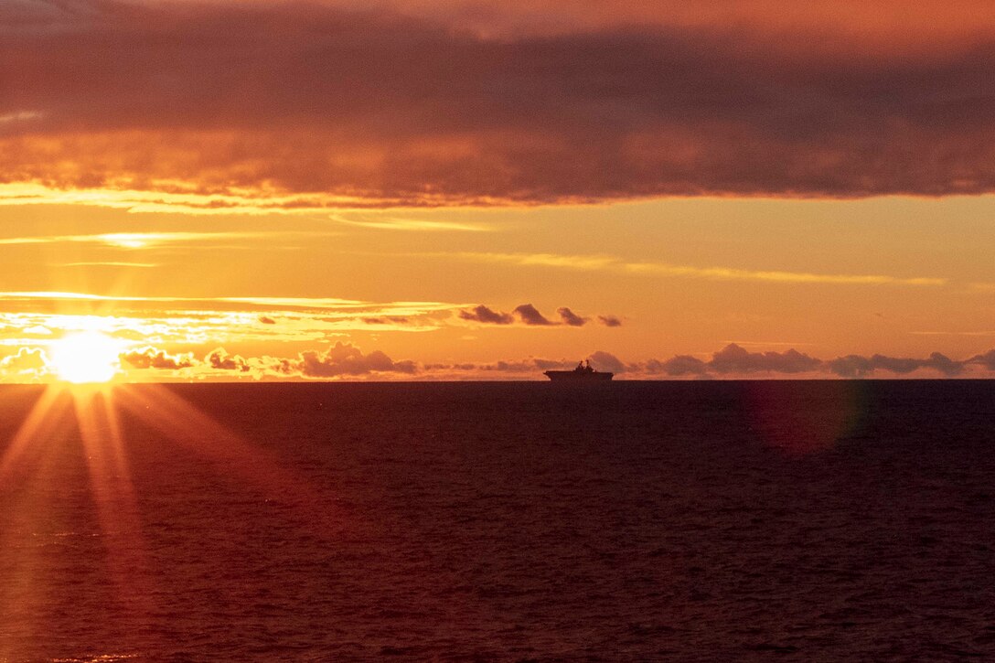 A ship sails as the sun rises on the horizon.