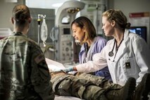 Two doctors with a soldier on the table and one soldier standing by.