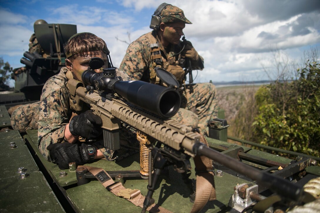 A Marine points a weapon while another Marine kneels next to him.