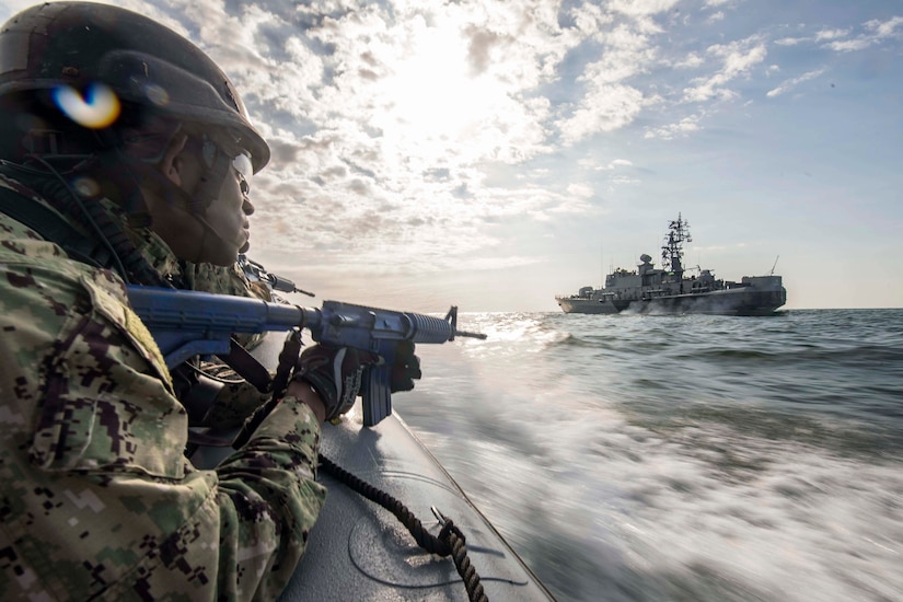 A sailor rides in an inflatable boat looking out towards a ship.