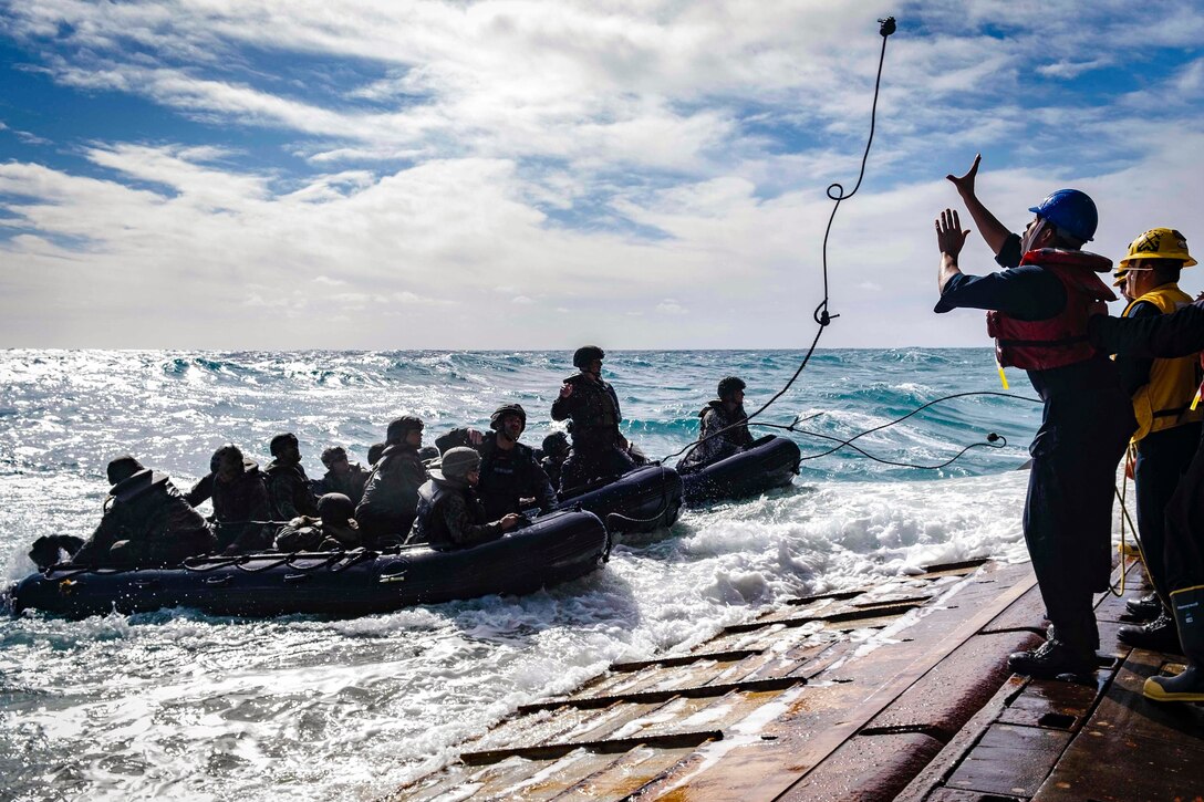 A sailor attempts to catch a rope from Marines in a small boat.