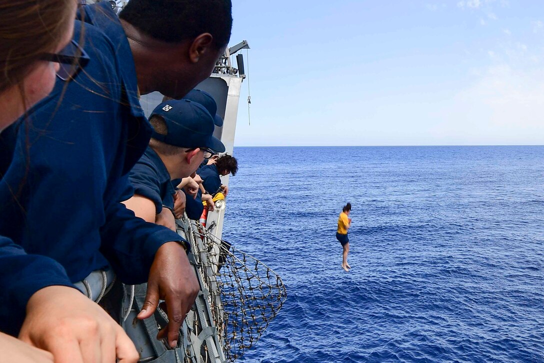 Sailors on a ship watch another jump into the ocean.