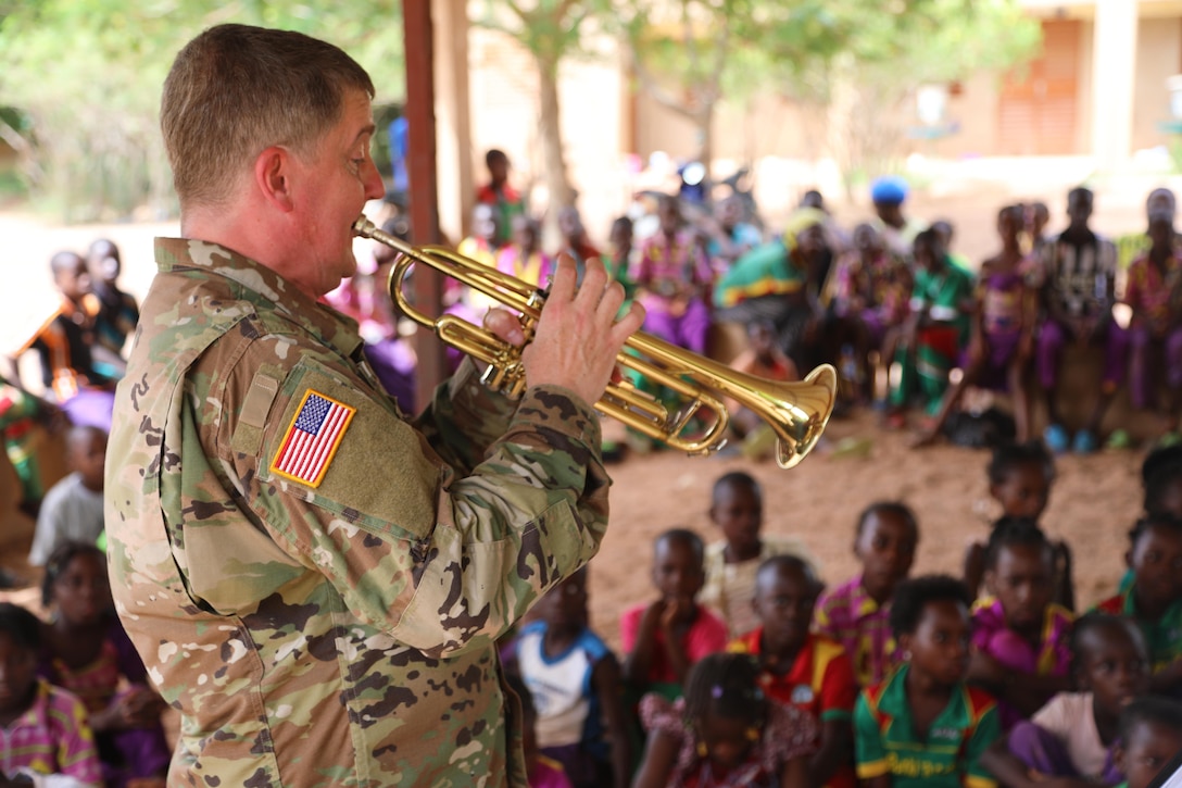 A soldier plays an instrument for children gathered around.