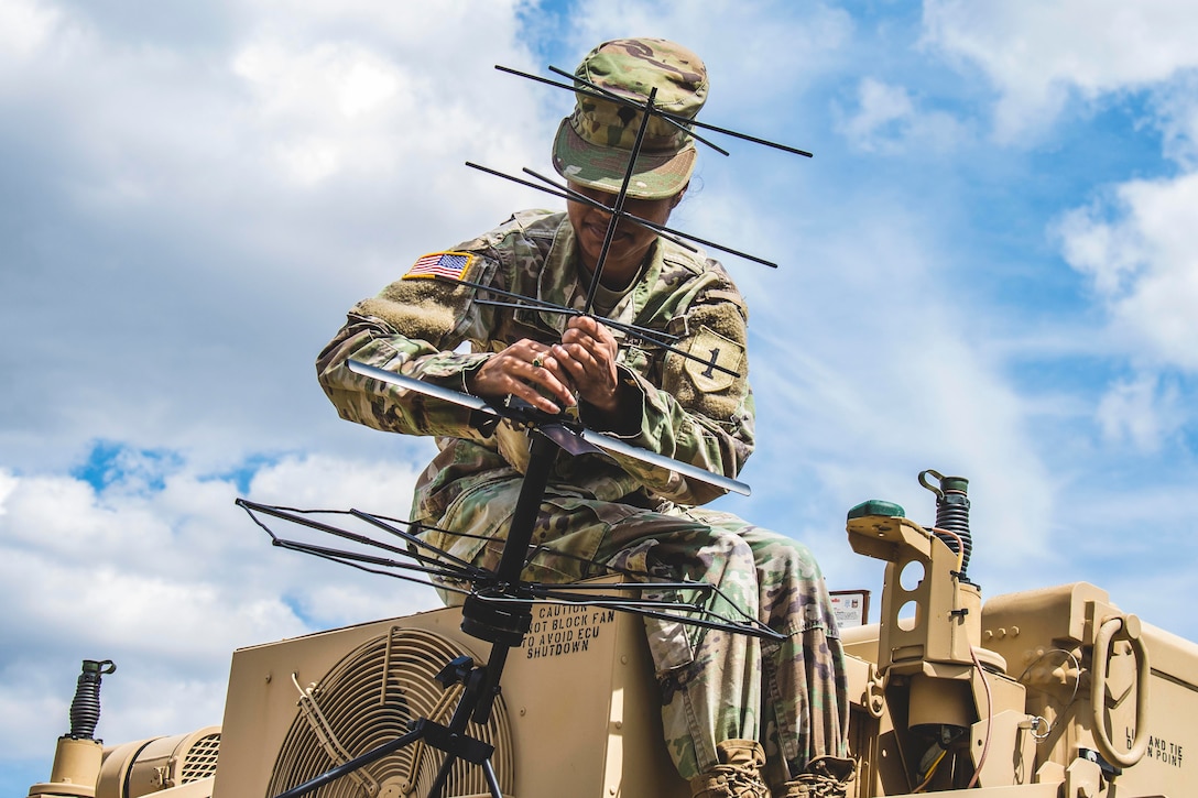 A solider adjusts an antenna on top of a military vehicle.