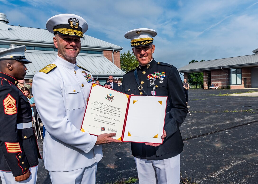 Navy rear admiral lower half presenting a retirement certificate to a Marine Corps lieutenant colonel during a retirement ceremony.