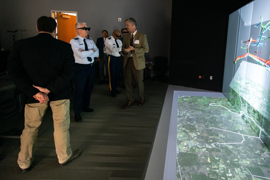 A man in uniform wears dark glasses while looking at a large screen.