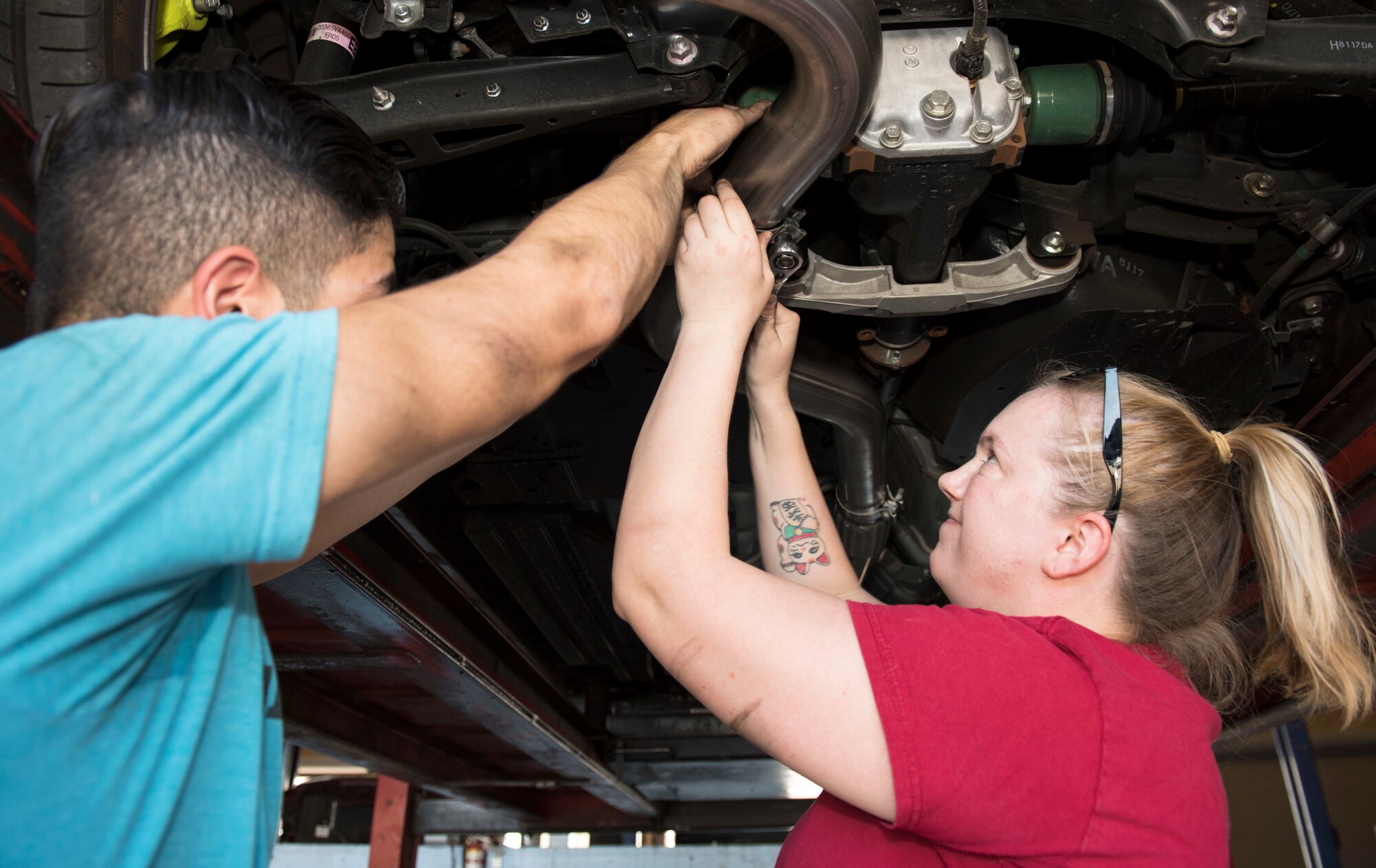 Senior Airman Igor Pacheco, 56th Medical Support Squadron lab technician (left), and Senior Airman Samantha Campbell, 56th Civil Engineer Squadron Airman dorm leader, work together to replace an exhaust system in a vehicle June 29, 2019, in the Auto Hobby Shop at Luke Air Force Base, Ariz.