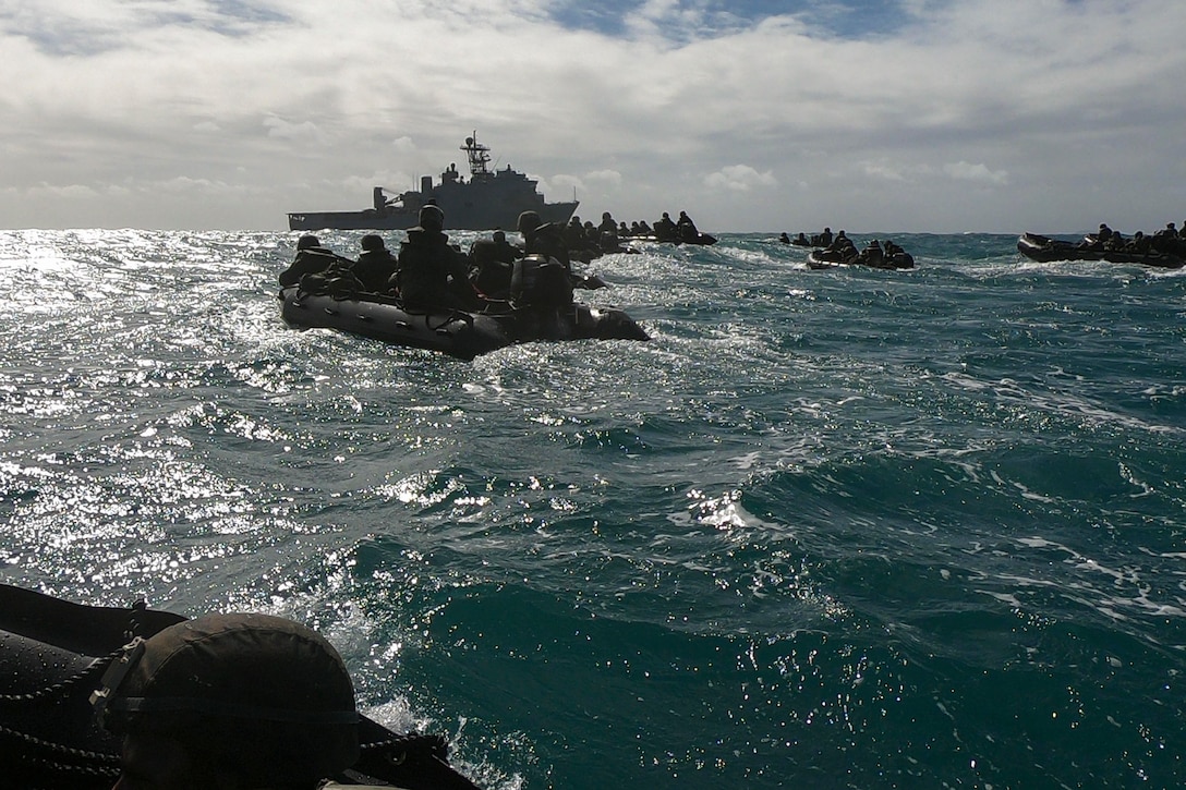 Several groups of Marines ride in small boats headed towards a large ship.