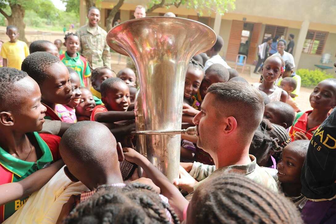 A soldier plays an instrument while surrounded by children.