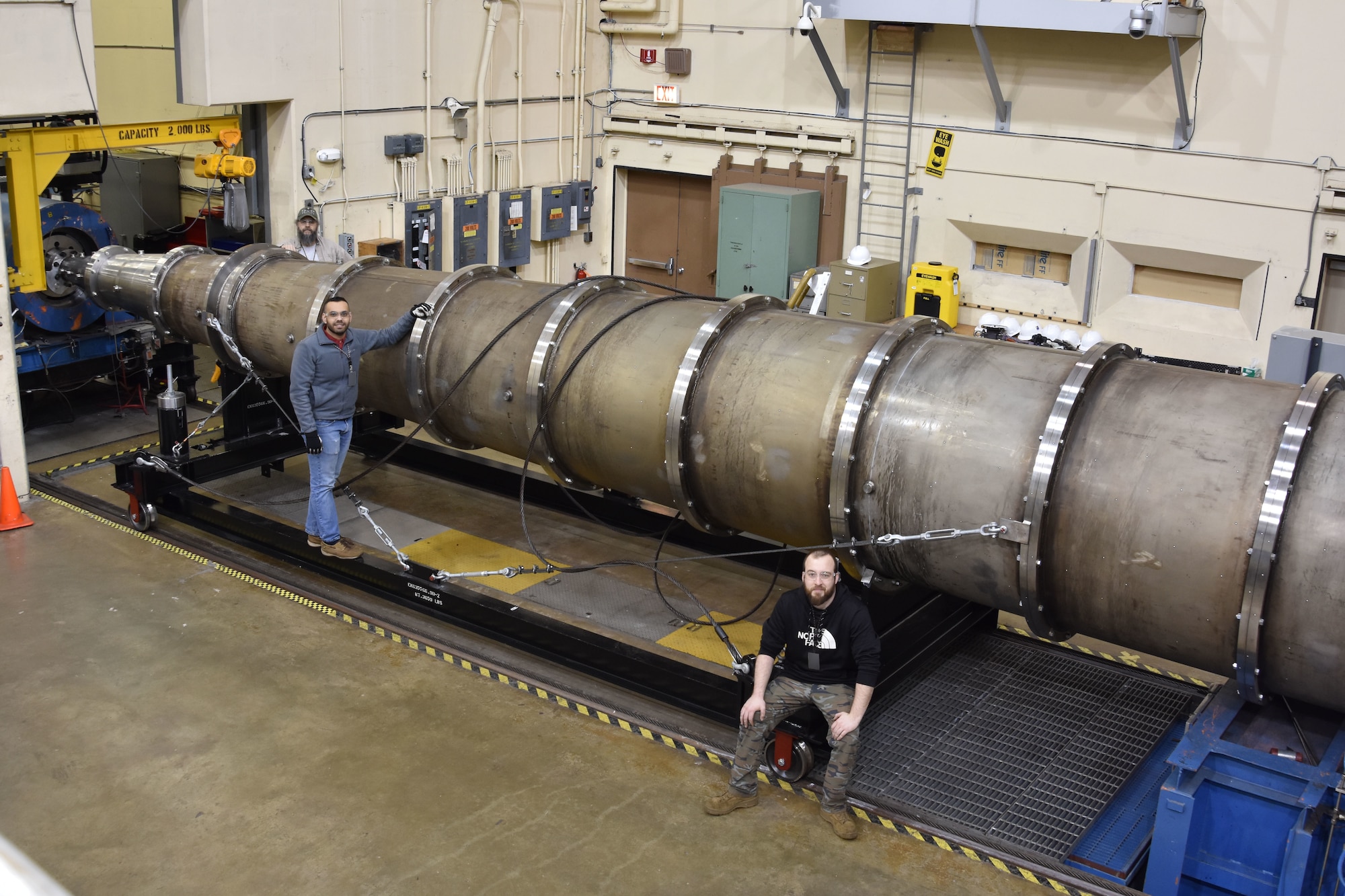 Rob Hale, engineering technician, left, Parth Kathrotiya, system engineer, center, and Zack Russo, engineering technician, pose with the Mach 18 nozzle at AEDC Hypervelocity Wind Tunnel 9 in White Oak, Maryland. The team at Tunnel 9 recently completed an initial shakeout of the Mach 18 system, and the calibration to bring Mach 18 to full operating capability is set to occur later this year. (U.S. Air Force photo by A.J. Spicer) (This image has been altered by obscuring badges for security purposes)