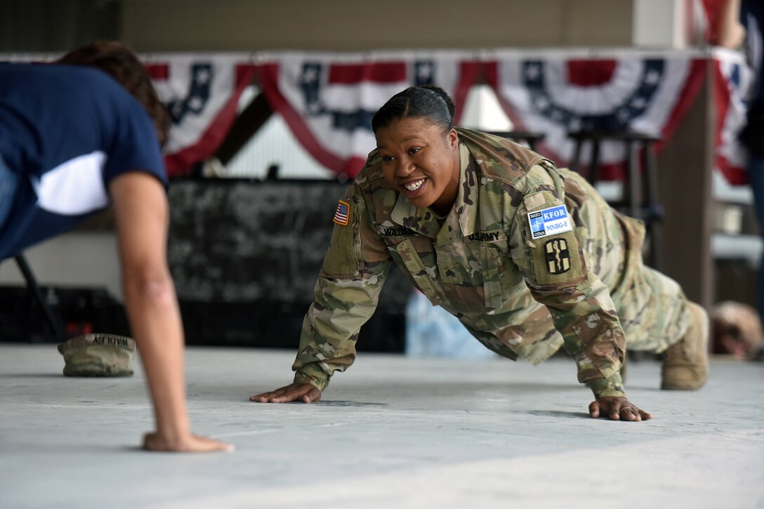 A soldier and an actress assume a plank position on the floor.