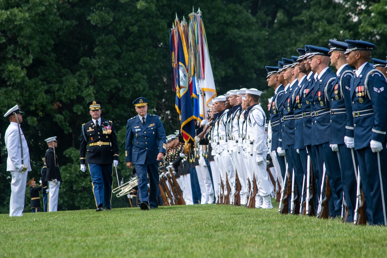 Military officers walk in front of a formation of troops.