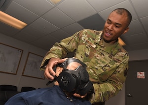 Staff Sgt. Aaron Harris, 50th Civil Engineer Squadron emergency management flight, demonstrates how to don an M-50 gas mask in the chemical, biological, radiological and nuclear training room at Schriever Air Force Base, Colorado, July 9, 2019. The flight supports the 50th Space Wing and 310th Space Wing, conducting thorough CBRN classes and ensuring all instructors have the appropriate qualifications. (U.S. Air Force Photo Illustration by Staff Sgt. Matthew Coleman-Foster)
