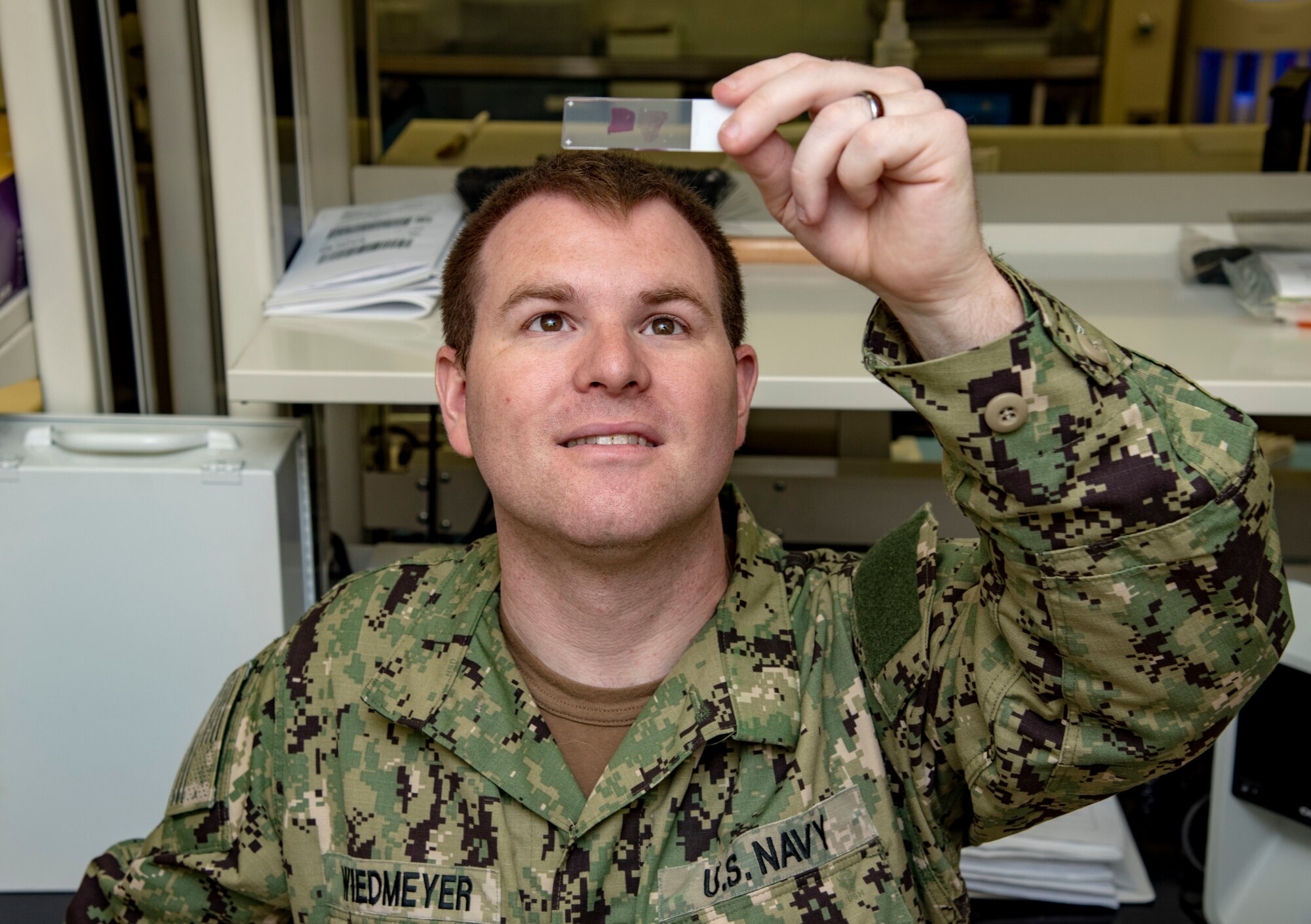 U.S. Navy Petty Officer 2nd Class Tyler Wiedmeyer, Armed Forces Medical Examiner System histotechnichian, looks at a slide of tissue before handing them off to a medical examiner June 6, 2019. The stained tissues help medical examiners see down to the cellular level for a diagnosis of cause of death. (U.S. Air Force photo by Staff Sgt. Nicole Leidholm)