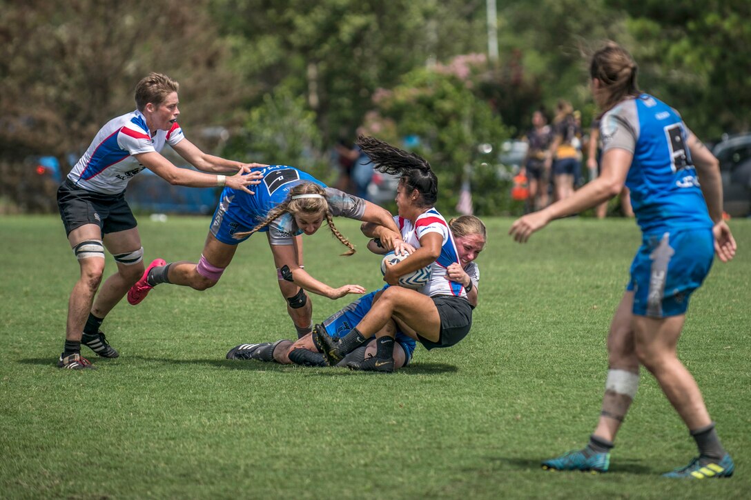 Two rugby players tackle a third as two other players approach.