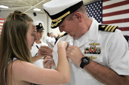 IMAGE: (Left to right) Cmdr. Joseph Oravec’s daughter pins the Commanding Officer Ashore pin to her father’s shirt following Naval Surface Warfare Center Dahlgren Division, Dam Neck Activity’s change of command. More than 200 Sailors and guests attended a traditional ceremony at Naval Air Station (NAS) Oceana’s Center for Naval Aviation Technical Training Unit’s ceremonial hangar aboard NAS Oceana June 27 where Cmdr. Andrew Hoffman was relieved of command by Oravec. Oravec became the command’s 28th commanding officer.